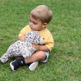 Little boy sitting on grass holding a harbour seal pup plush toy
